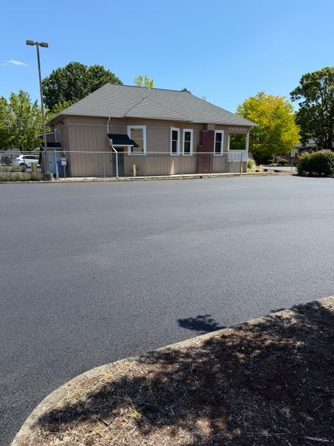 Small brick building with a gray roof beside an empty parking lot on a sunny day
