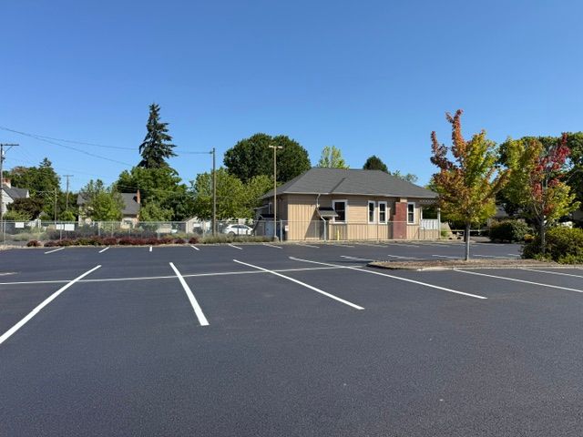 Empty parking lot with white lines, a small building, and trees under a clear blue sky