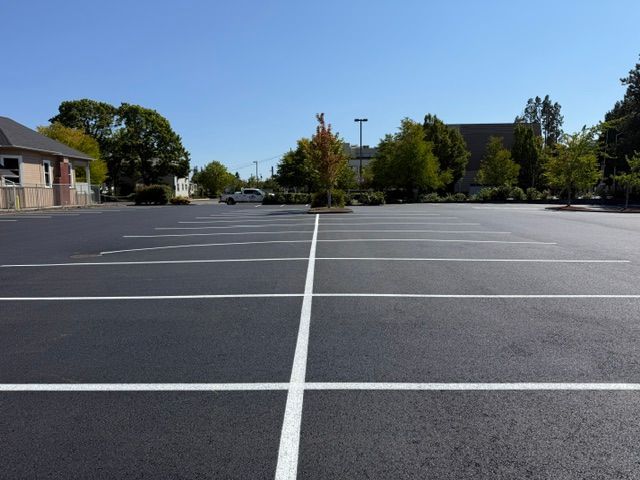 Empty parking lot with white lane markings under a clear blue sky, buildings and trees in the background