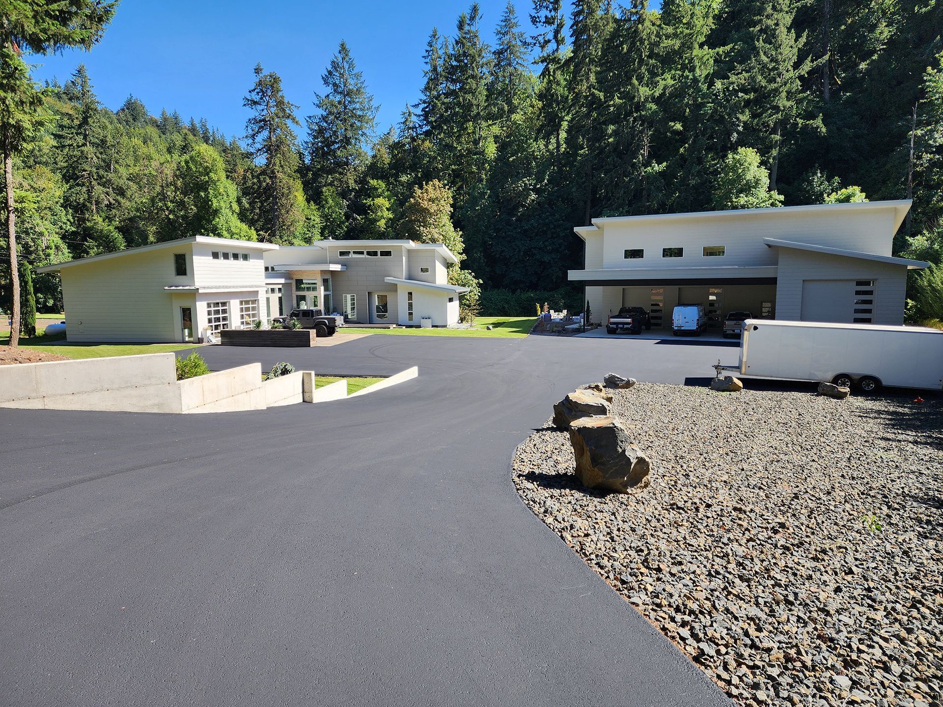 Modern houses with curved white walls beside a paved driveway in a wooded area.