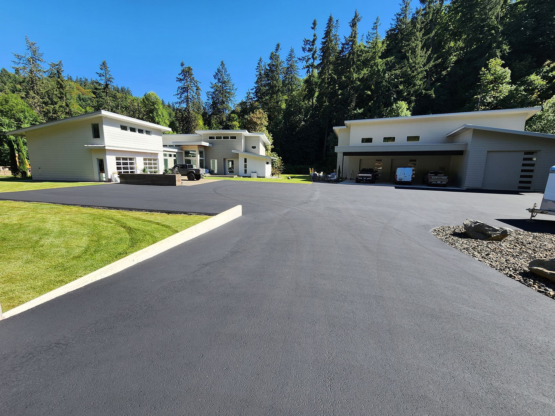 Paved driveway between white houses surrounded by trees under a clear blue sky