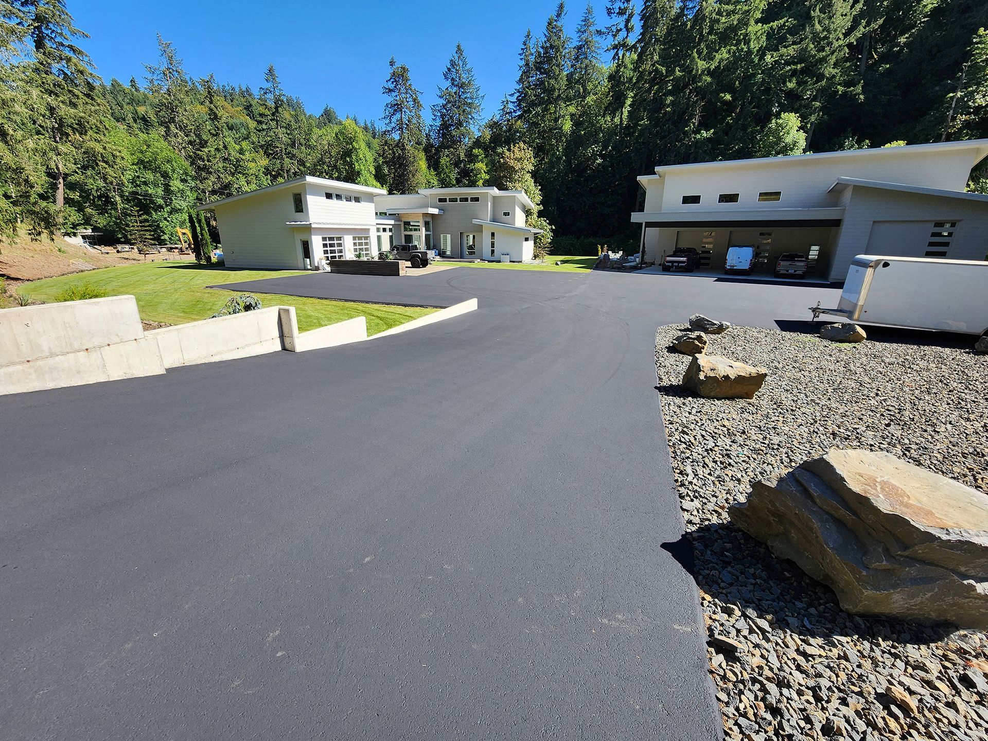 Paved driveway and modern house in a wooded residential area, with large rocks and a garage on the right.