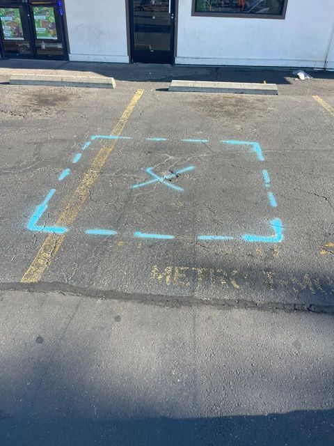 Blue chalk square with an X marked on an asphalt parking lot in front of a building.