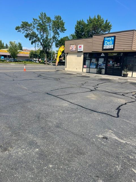 Small strip mall storefront with cracked asphalt parking lot and trees in the background.