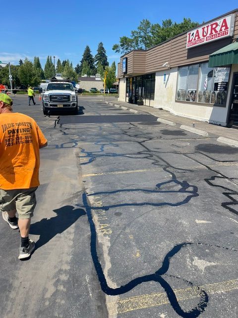 Man walking past a storefront on a cracked, freshly sealed parking lot under a clear blue sky