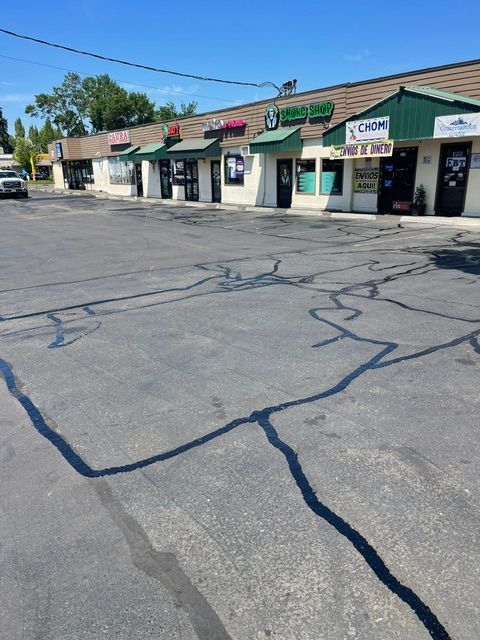 Sunlit strip mall storefronts behind a cracked asphalt parking lot under a clear blue sky