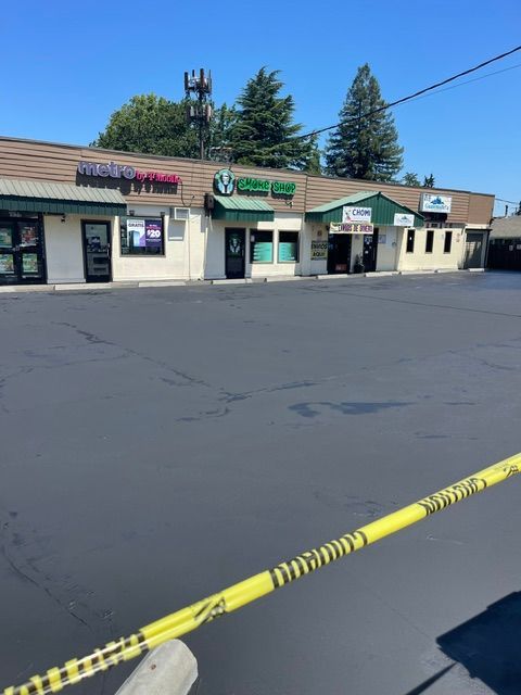Strip mall storefronts behind yellow caution tape across an empty parking lot on a sunny day