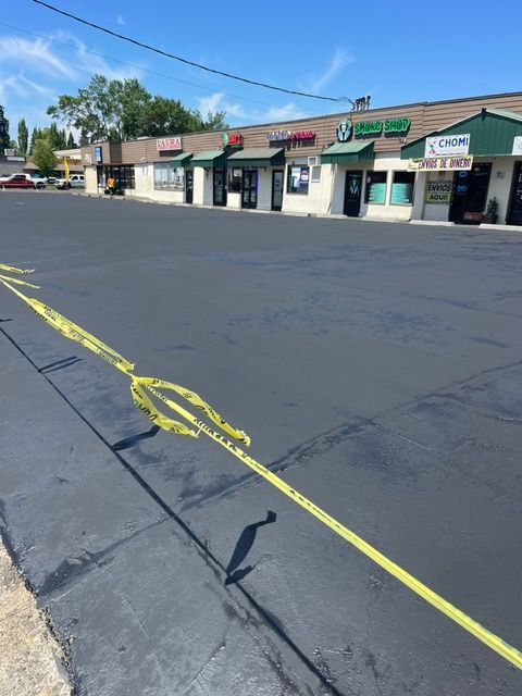 Strip mall storefronts with a cracked parking lot marked by yellow caution tape under a clear blue sky