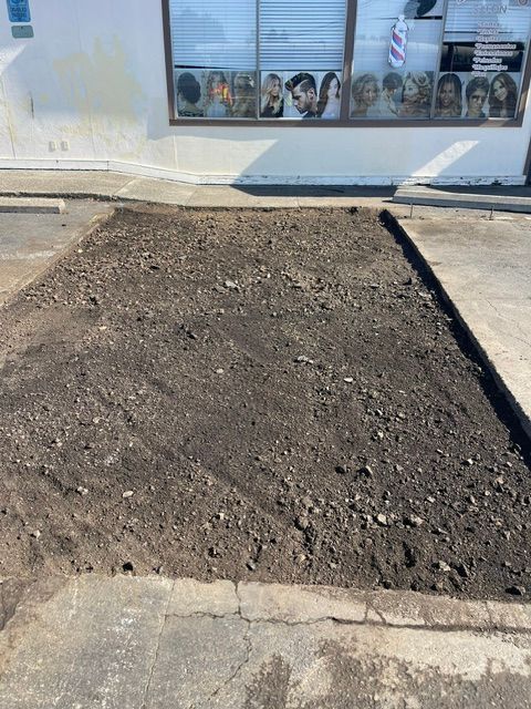 Freshly dug dirt patch beside a sidewalk in front of a storefront window