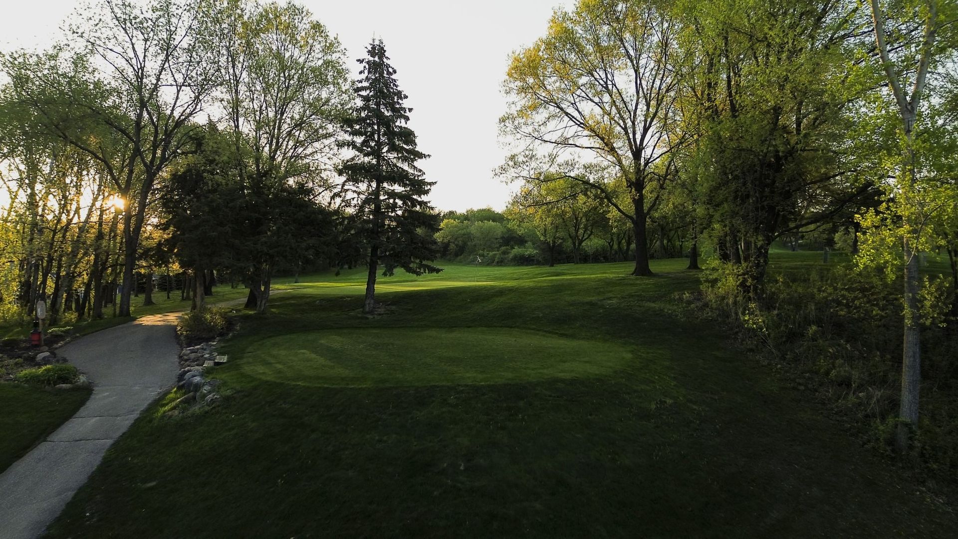 A golf course surrounded by trees and a path.