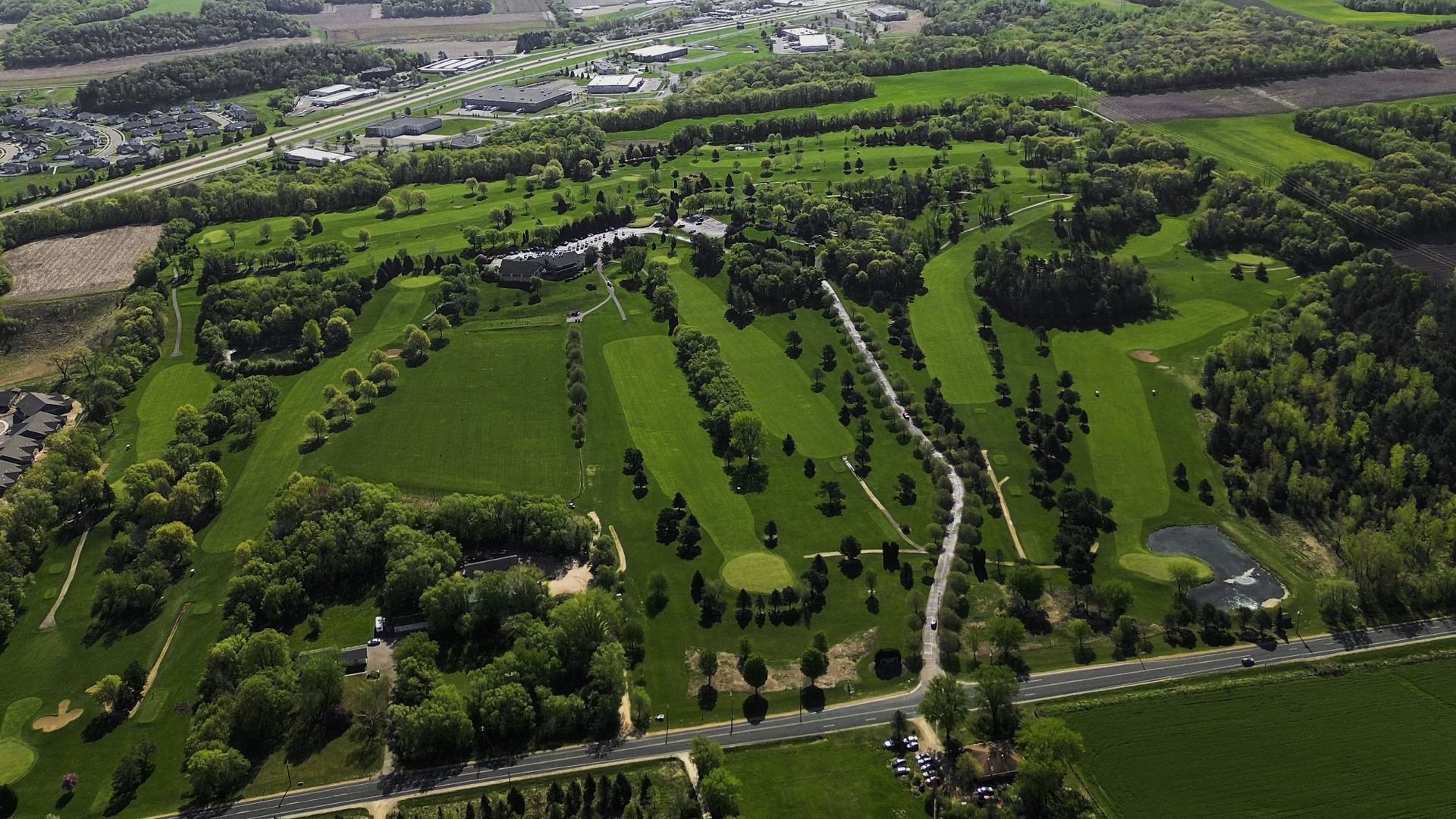 An aerial view of a golf course surrounded by trees and fields