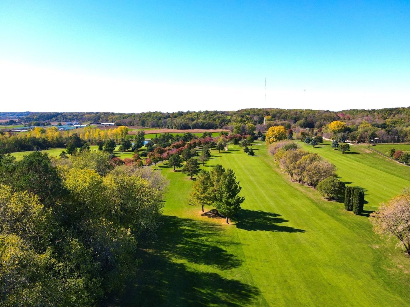 An aerial view of a golf course surrounded by trees on a sunny day.