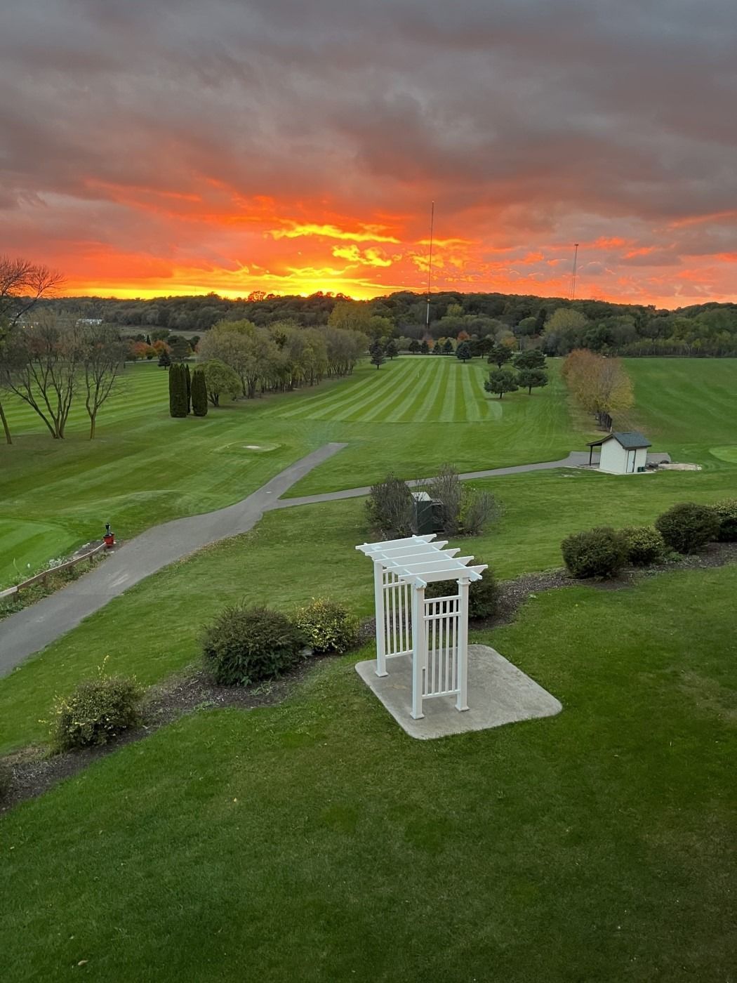 A sunset over a golf course with a white pergola in the foreground.