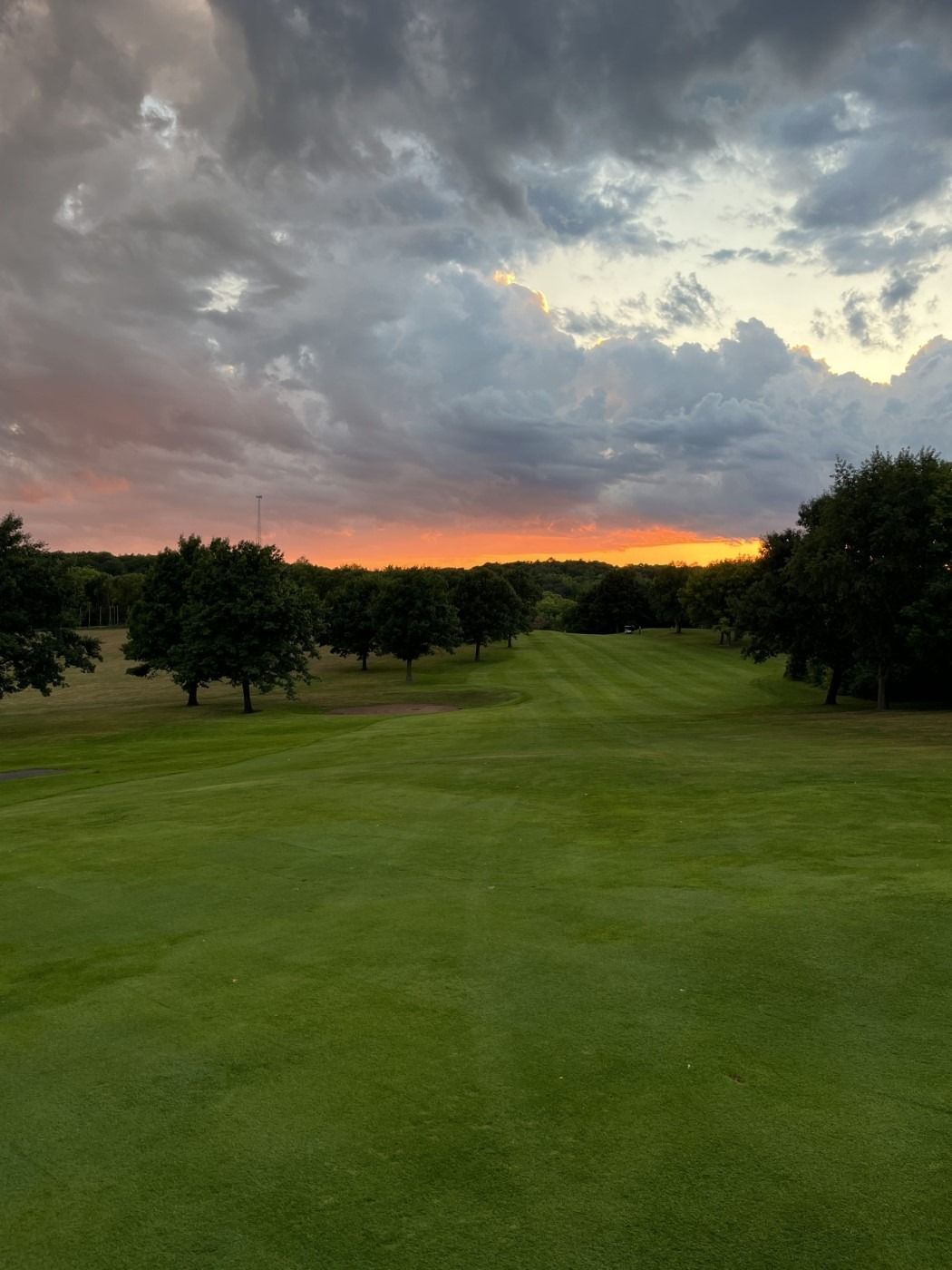 A golf course with a sunset in the background and trees in the foreground.