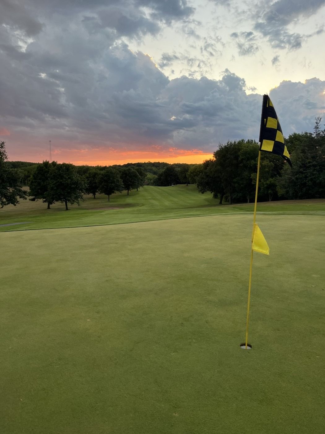 A yellow and black flag on a golf course with a sunset in the background