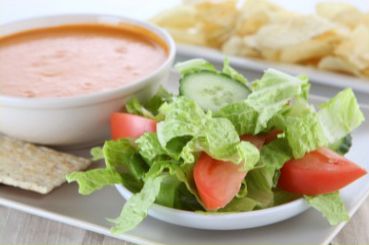 Soup, salad, and chips on a white platter; tomatoes, cucumber, lettuce, and reddish soup.