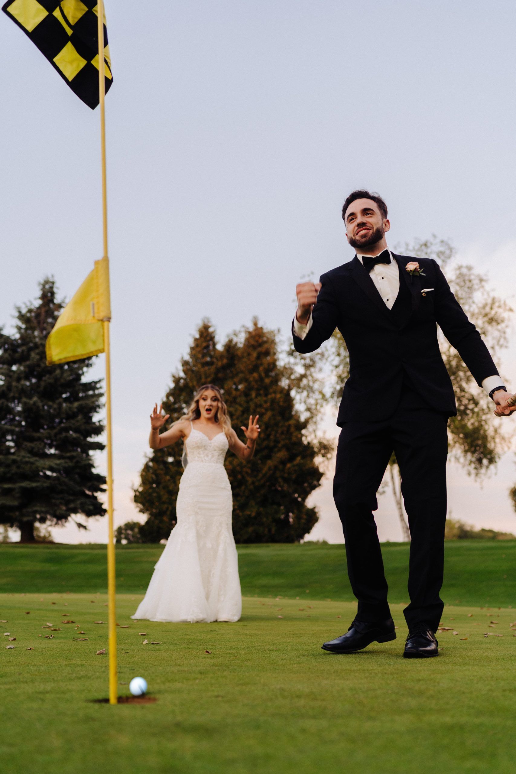 Newlyweds celebrate on a golf course. The groom raises a fist, and the bride gives thumbs up.