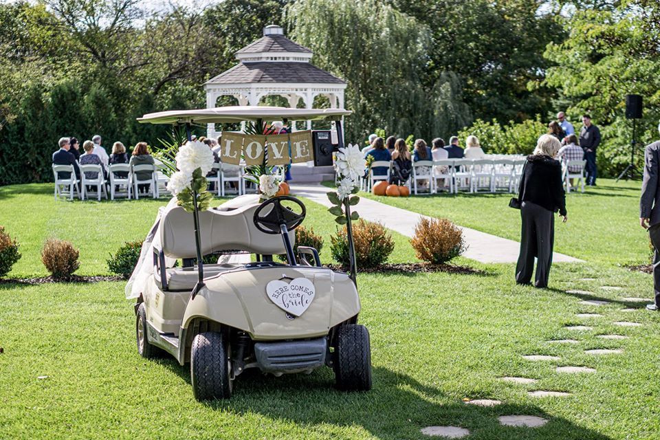 Golf cart decorated for a wedding, gazebo and guests in background.