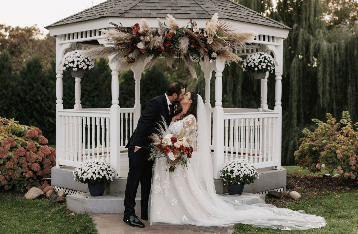 Bride and groom kissing under a decorated gazebo at their wedding.