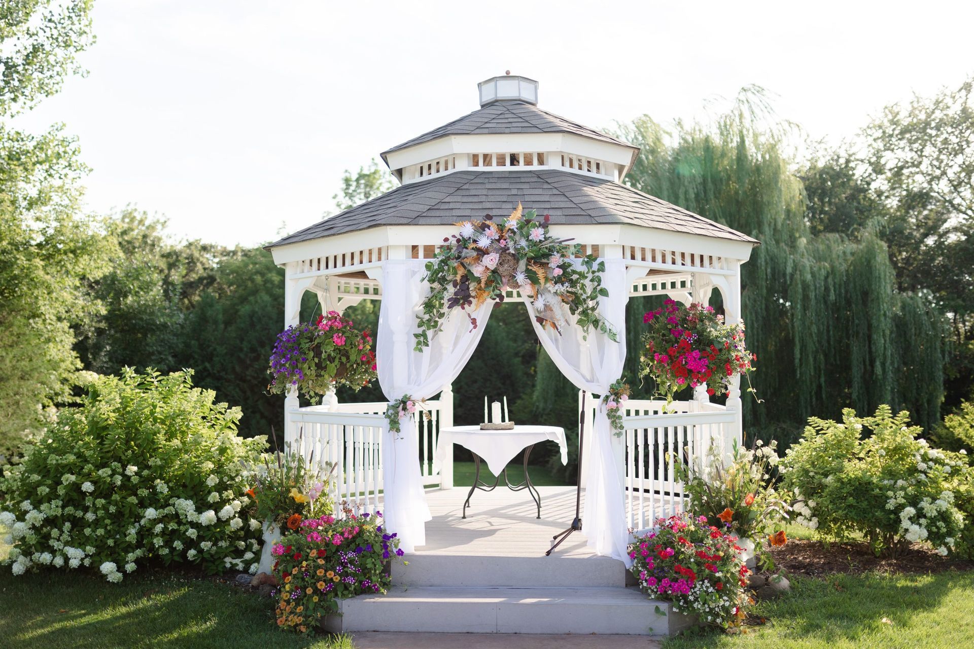 White gazebo decorated with flowers for an outdoor wedding ceremony.