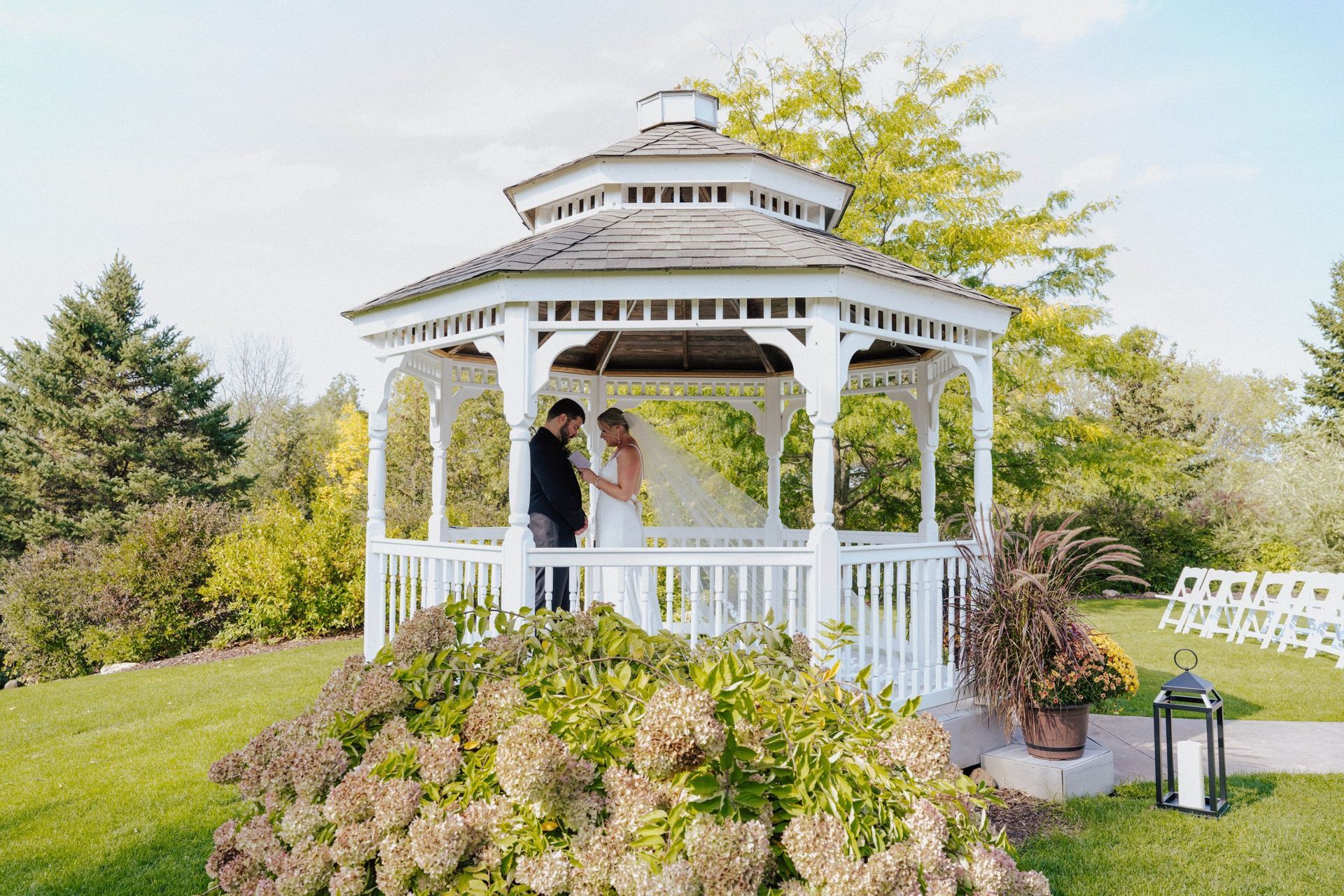 Bride and groom in a white gazebo on a sunny day; wedding ceremony.
