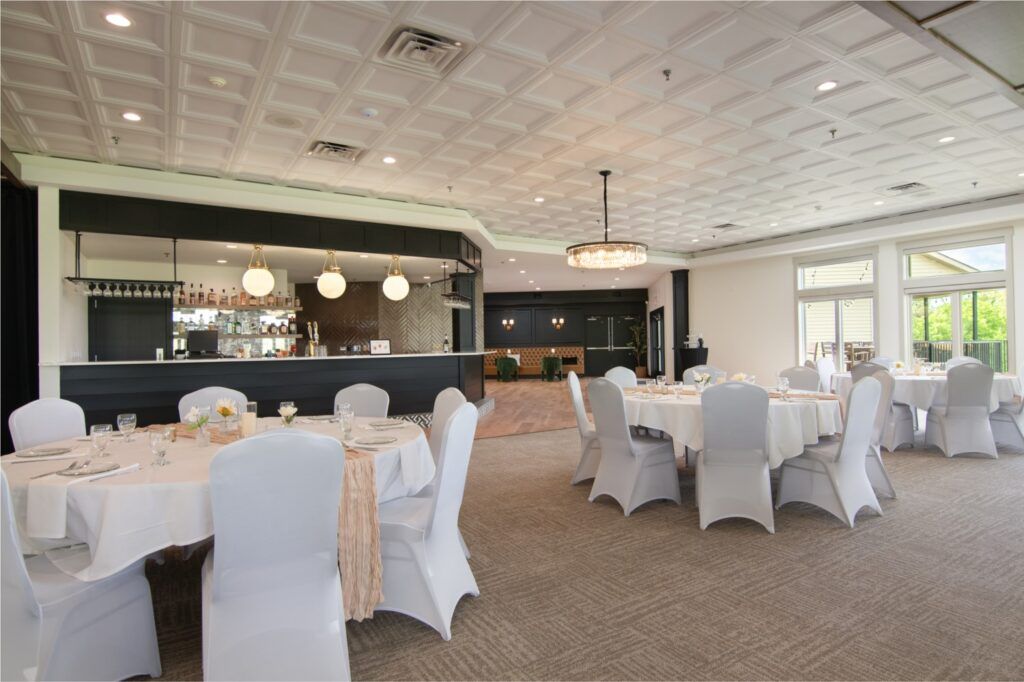 Banquet hall: round tables with white covers, bar in background, white ceiling.