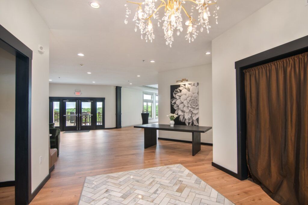Hallway with wooden floor, black trimmed doors, and an abstract painting. Bright chandelier overhead.