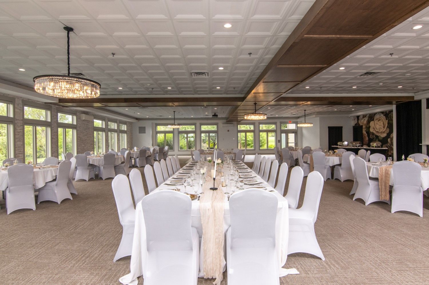 Elegant banquet hall with white tablecloths, chairs, and tables, a long center table, and a neutral-toned color scheme.