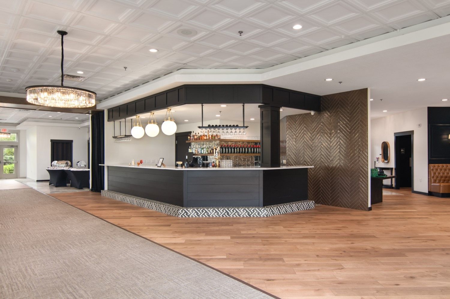 Bar area with a black counter, light wood floors, and patterned ceiling tiles.