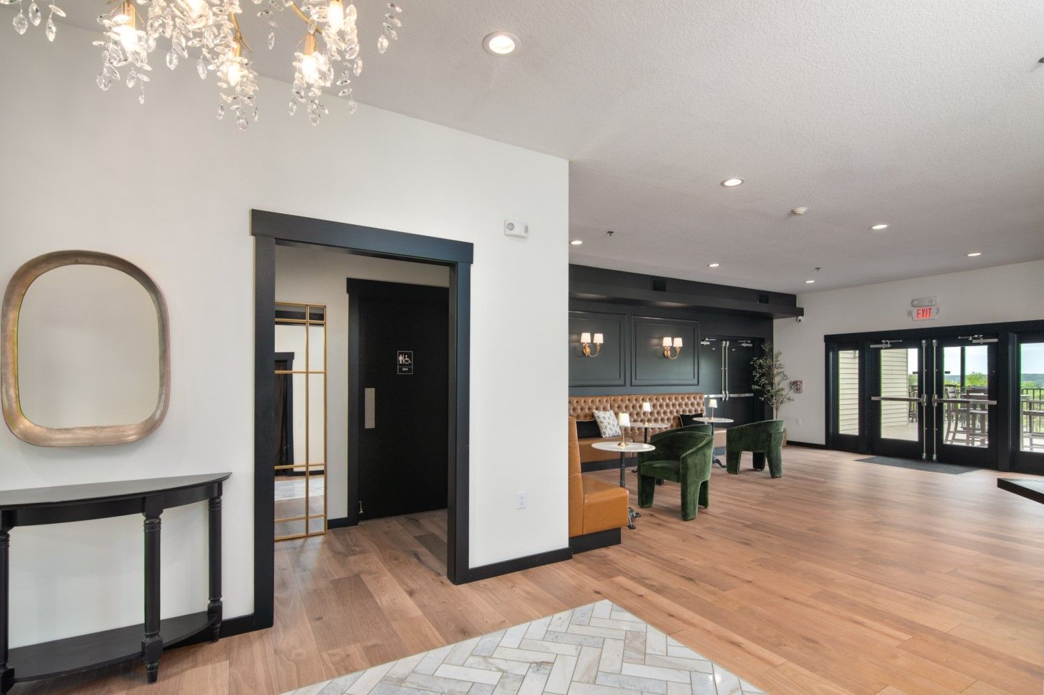 Lobby with wood floor, black door, gold mirror, and dining nook with green chairs.