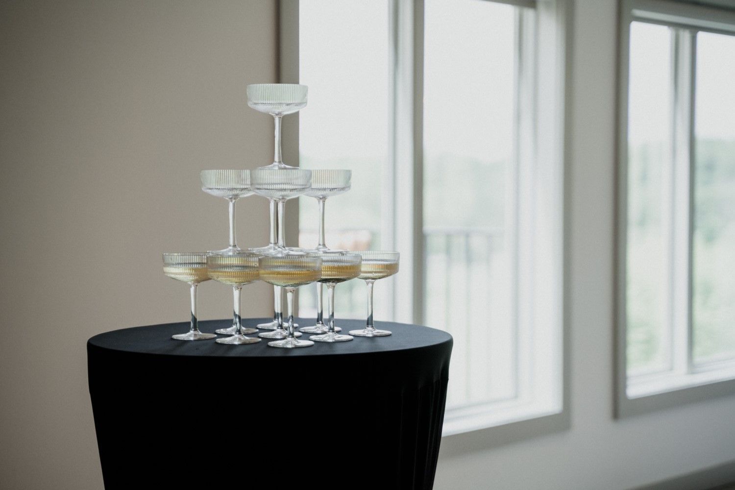 Champagne glasses stacked in a pyramid on a black-covered table, near a window.