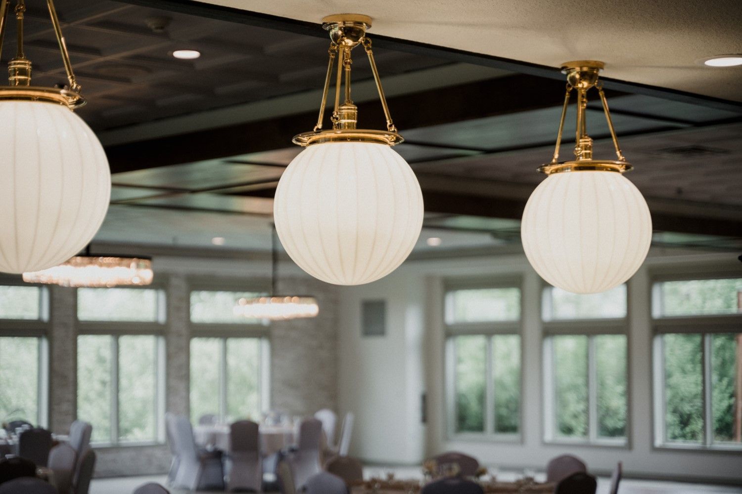 Three spherical, white pendant lights hang from a ceiling. Bright, open room with windows in background.