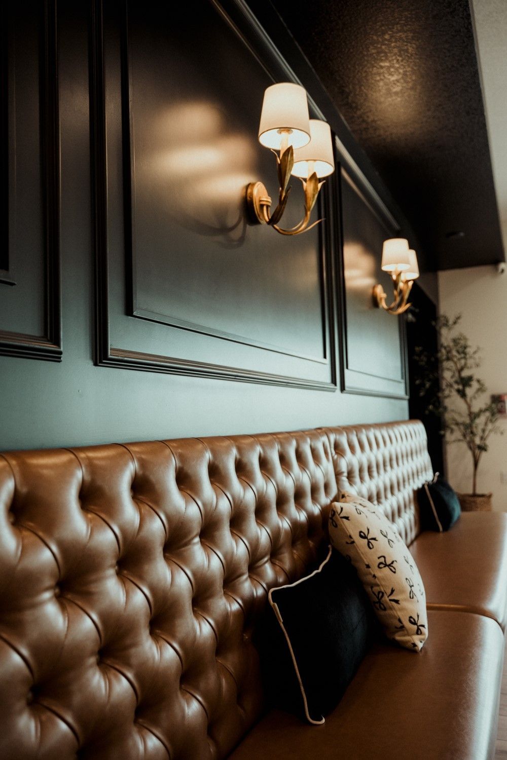 Brown leather tufted couch against a dark wall with sconce lighting and pillows.