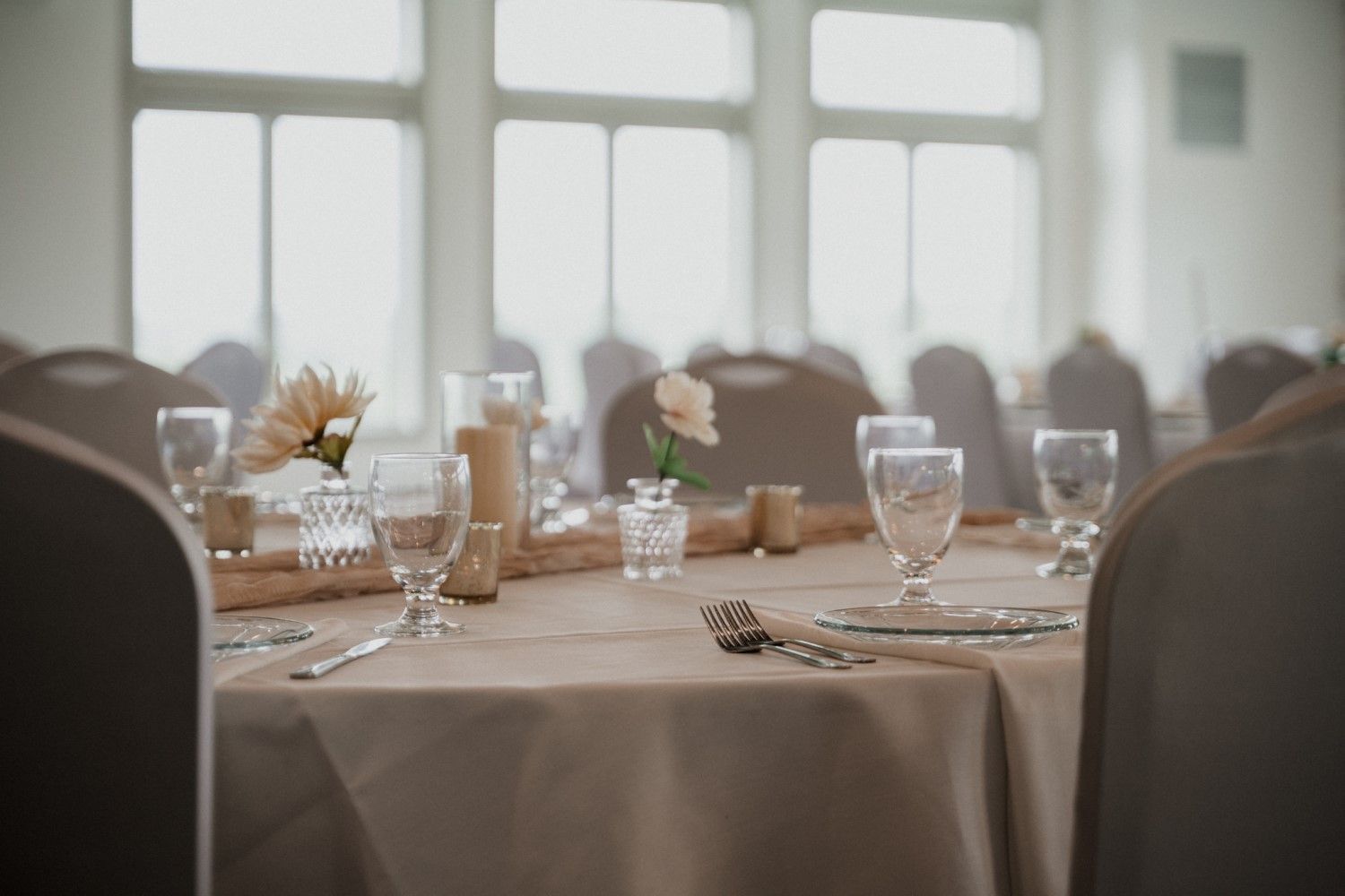 Round table set for a formal event, with flowers, glassware, and silverware.