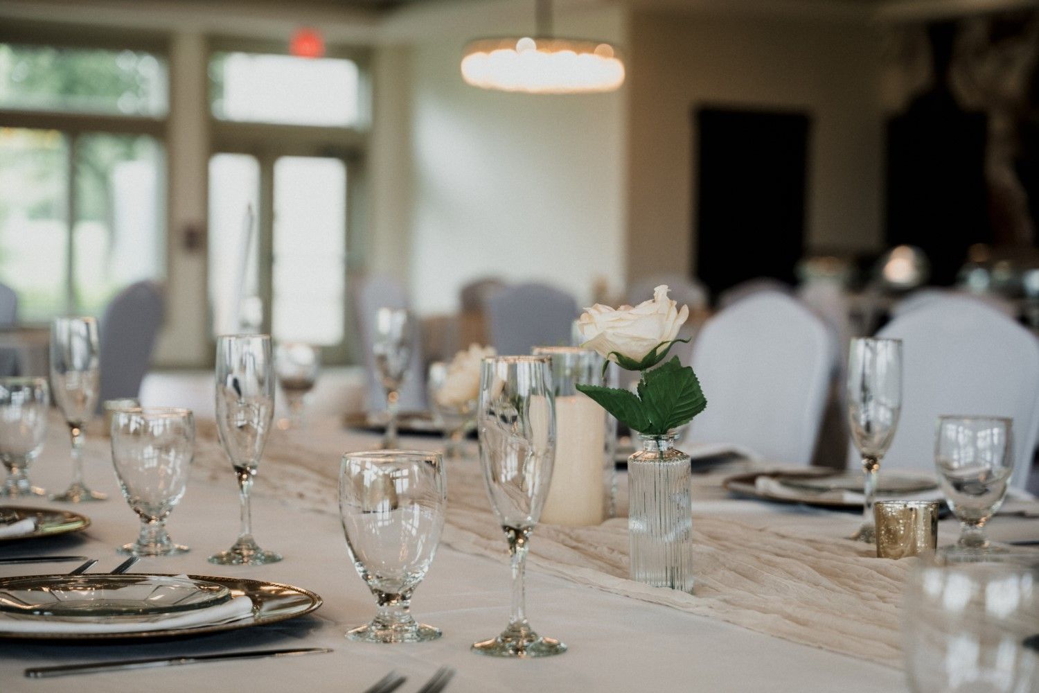 Wedding reception table setting with champagne flutes, plates, and a white rose.
