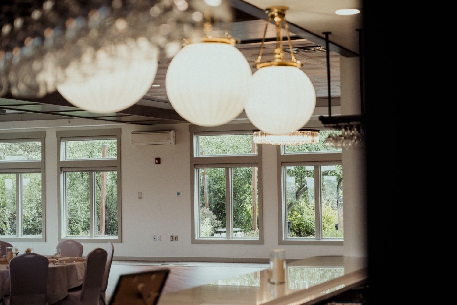 Three large, white globe lights hang over a room with tall windows overlooking greenery.