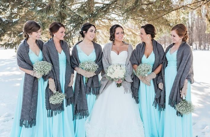 Bridesmaids in blue dresses and gray shawls with the bride in a snowy setting.