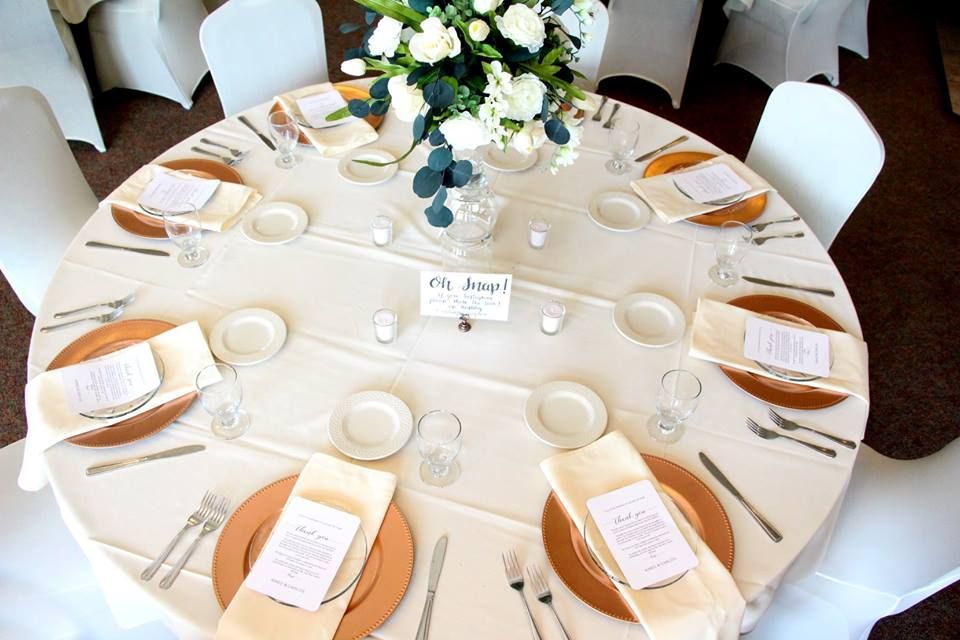Round table set for a formal event, featuring place settings, floral centerpiece, and name card.