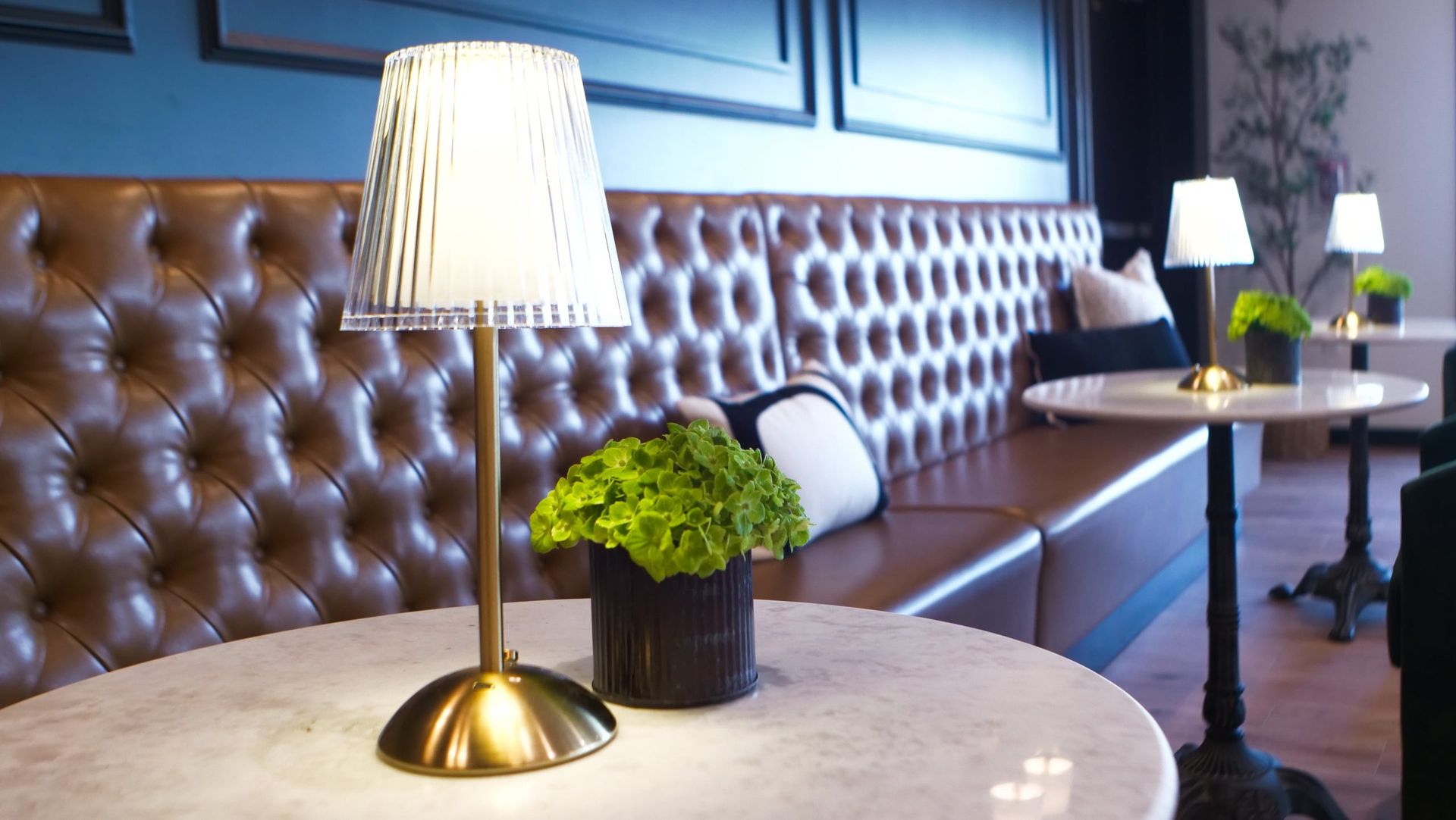 Table with lamp, green plant, and brown leather booth in a modern lounge setting.