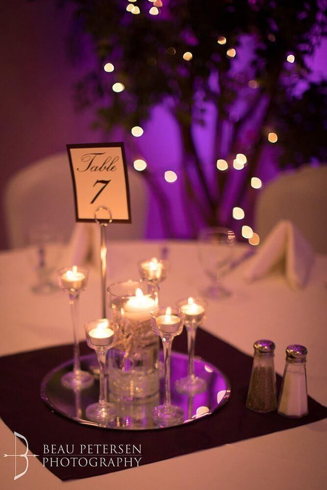 Table setting with candles and table number 7 at a wedding, with purple uplighting.