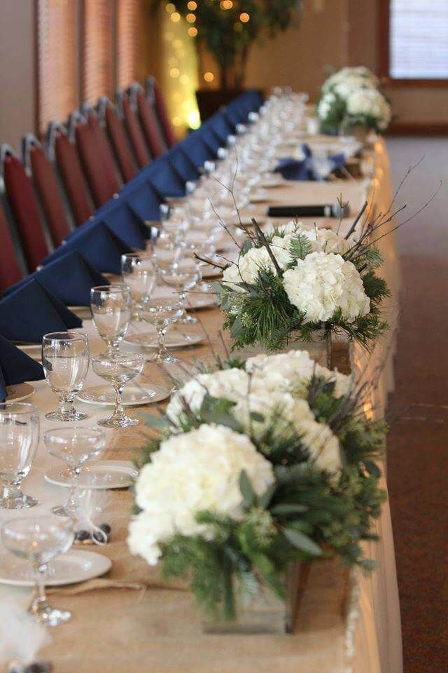 Long table set for a formal event with white floral centerpieces, navy napkins, and clear glassware.