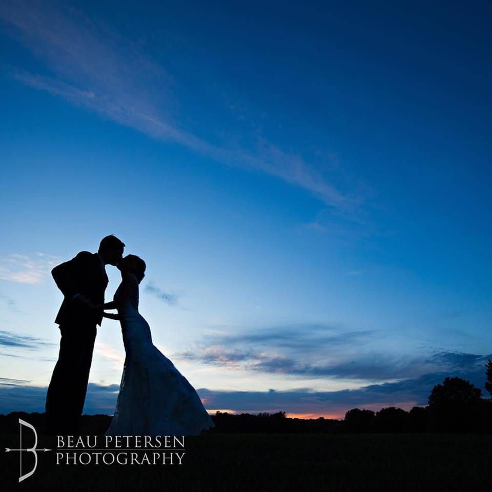 Silhouette of a kissing bride and groom at dusk against a blue and orange sky.