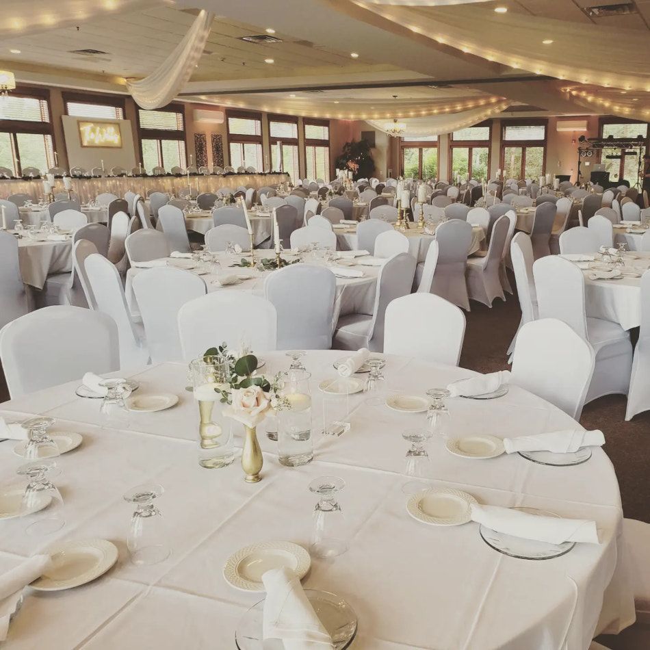 Large banquet hall set for a wedding reception; white linens, chairs with white covers, round tables with centerpieces.