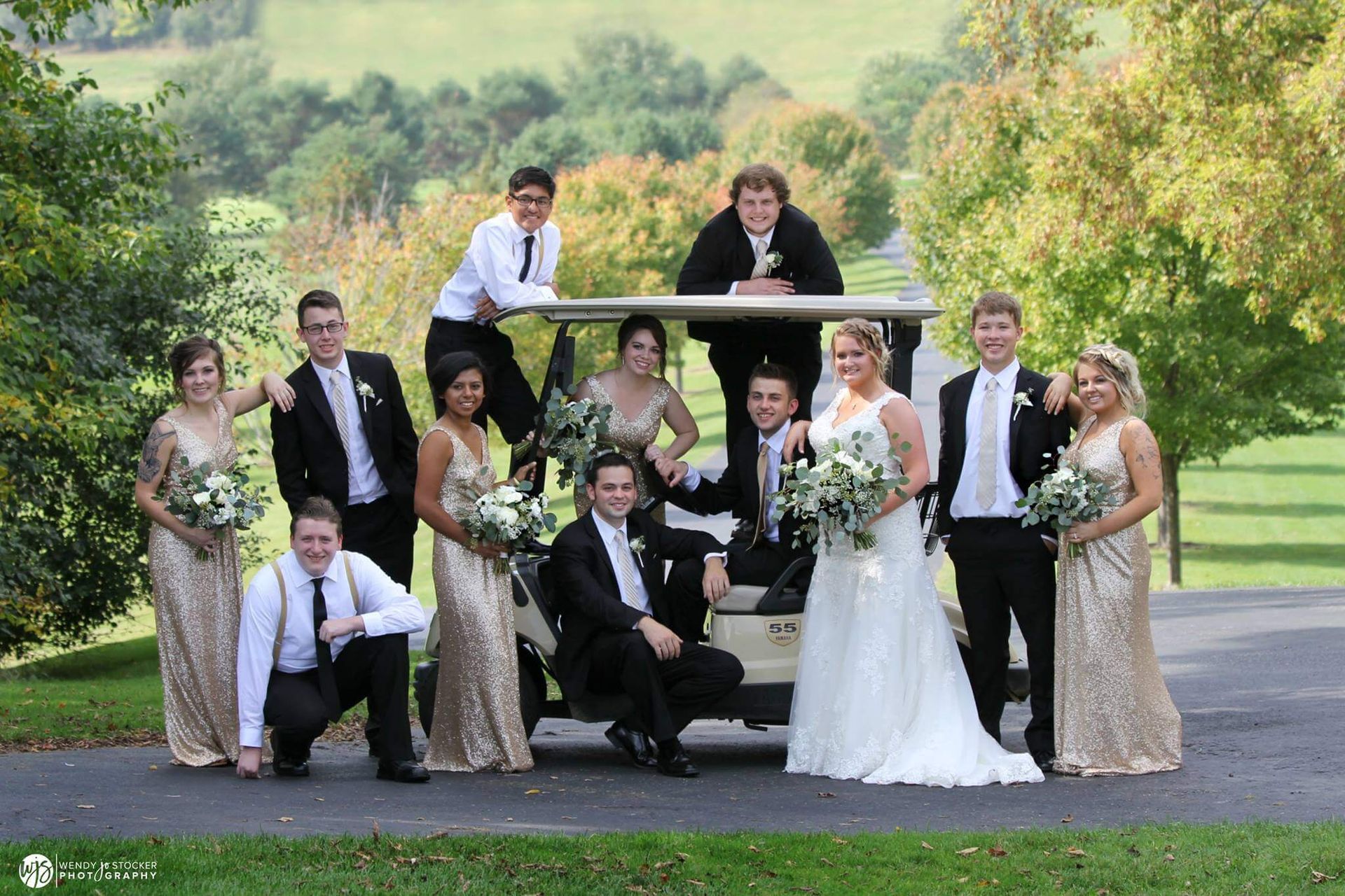 Wedding party posing with a golf cart in a park. Formal attire, smiling.