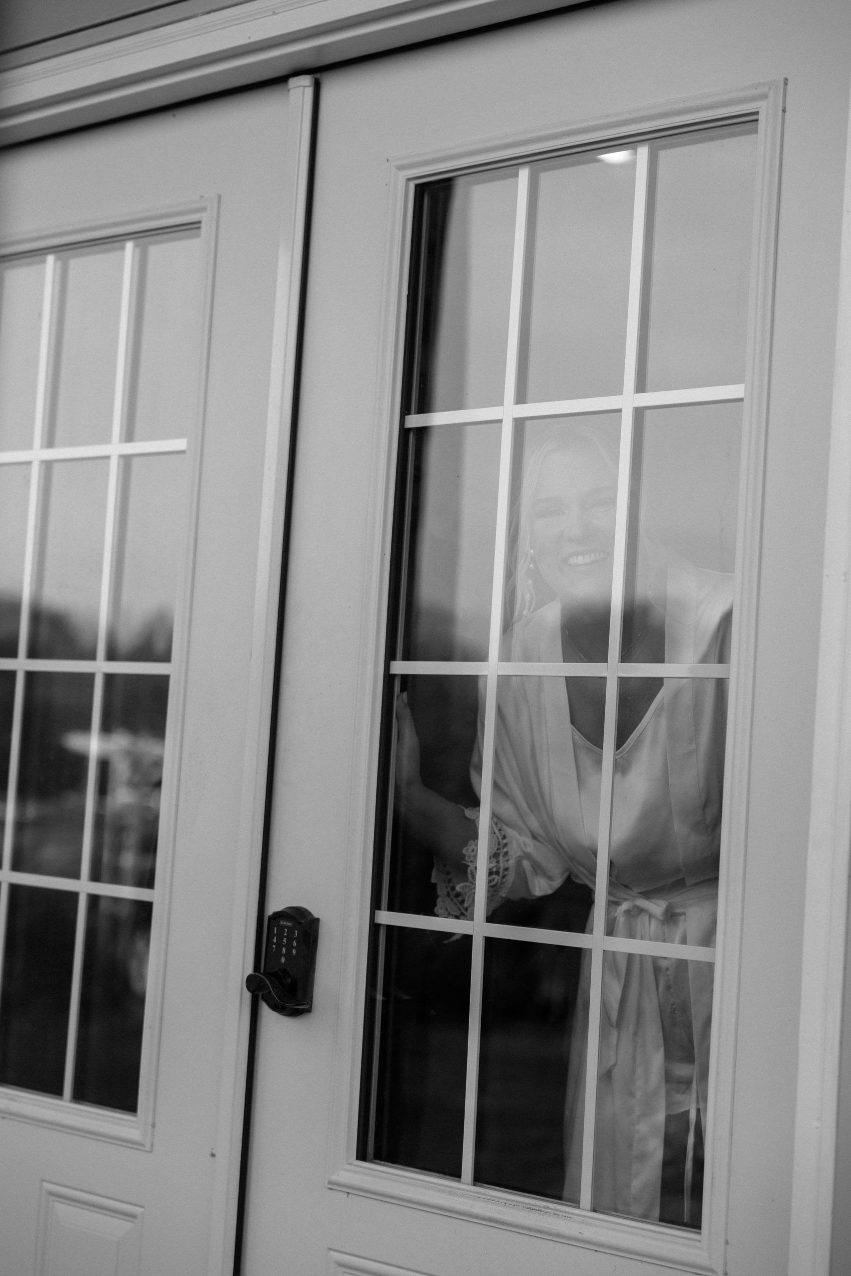 Woman smiling through a glass door with a grid pattern, in a white frame. Black and white.