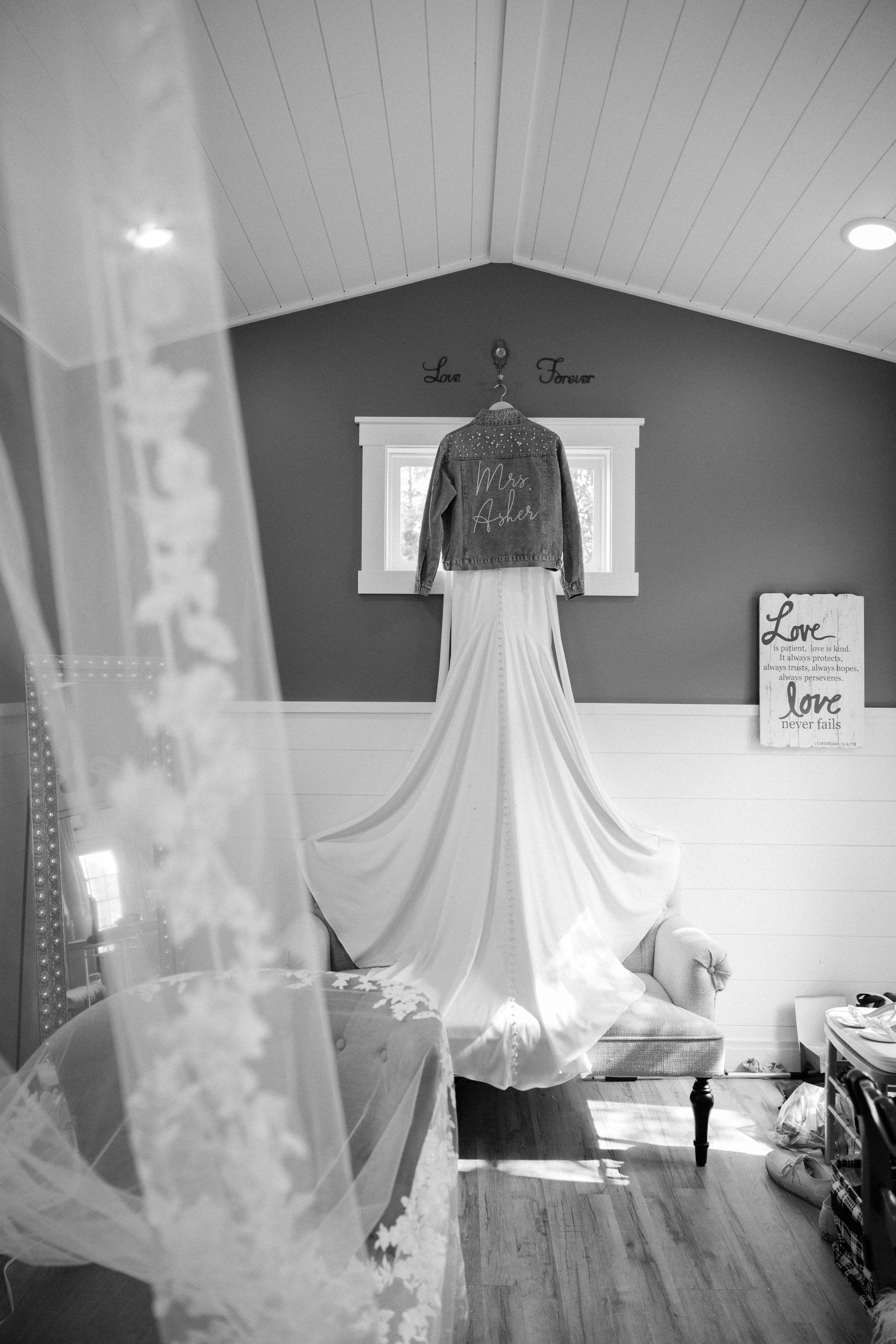 Wedding dress hanging with a denim jacket; veil in foreground.