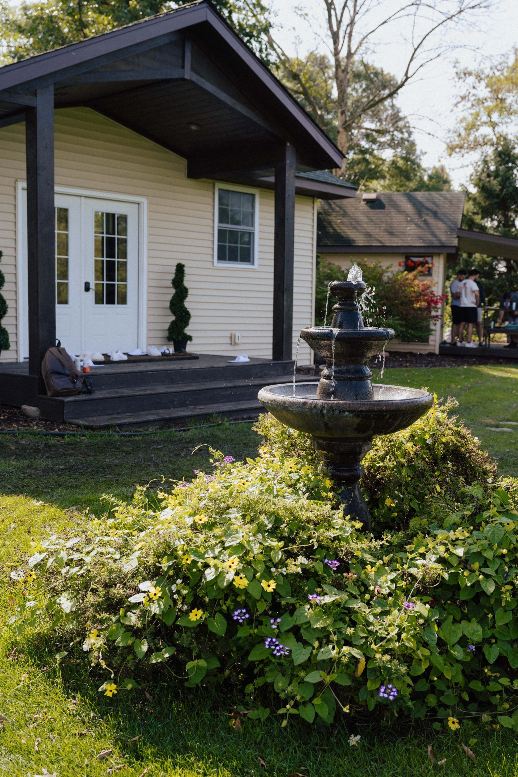 A house with a fountain in the yard. Green lawn and bushes surround a tiered fountain.