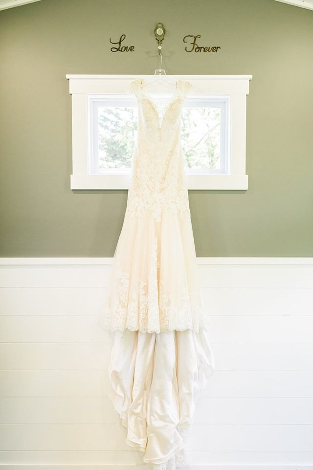 Wedding dress hanging on a hanger in front of a window. White and cream colors.