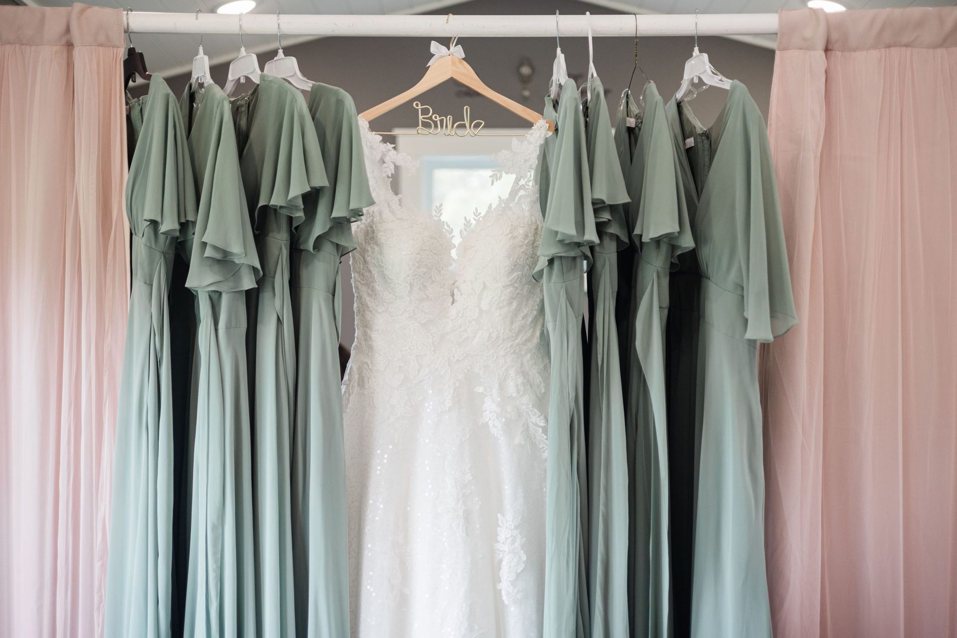Wedding dresses hanging, surrounded by sage green bridesmaid dresses.