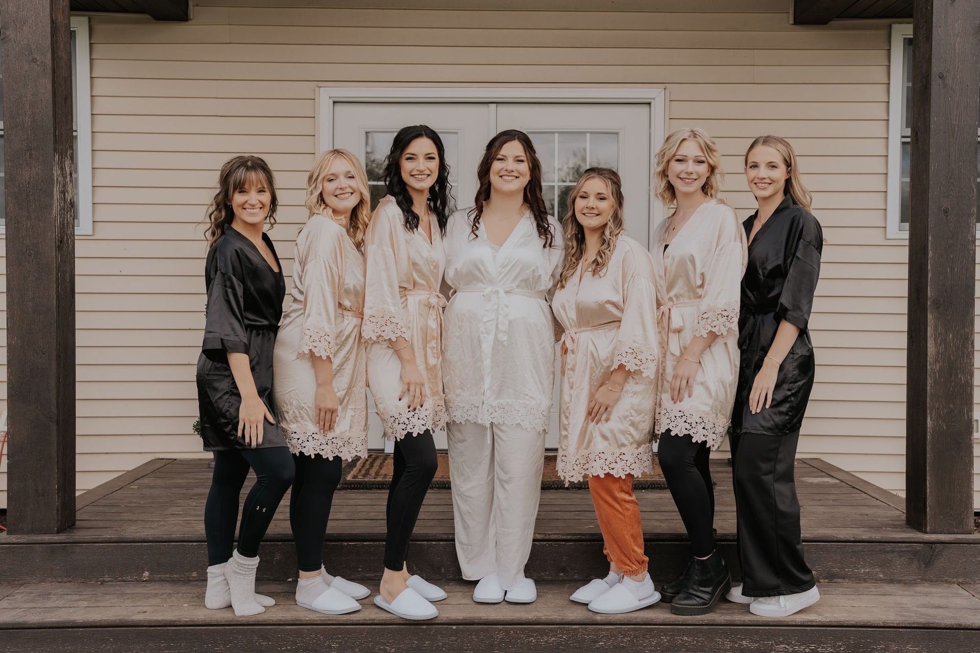 Bridesmaids in robes with the bride in white, posing on a porch.